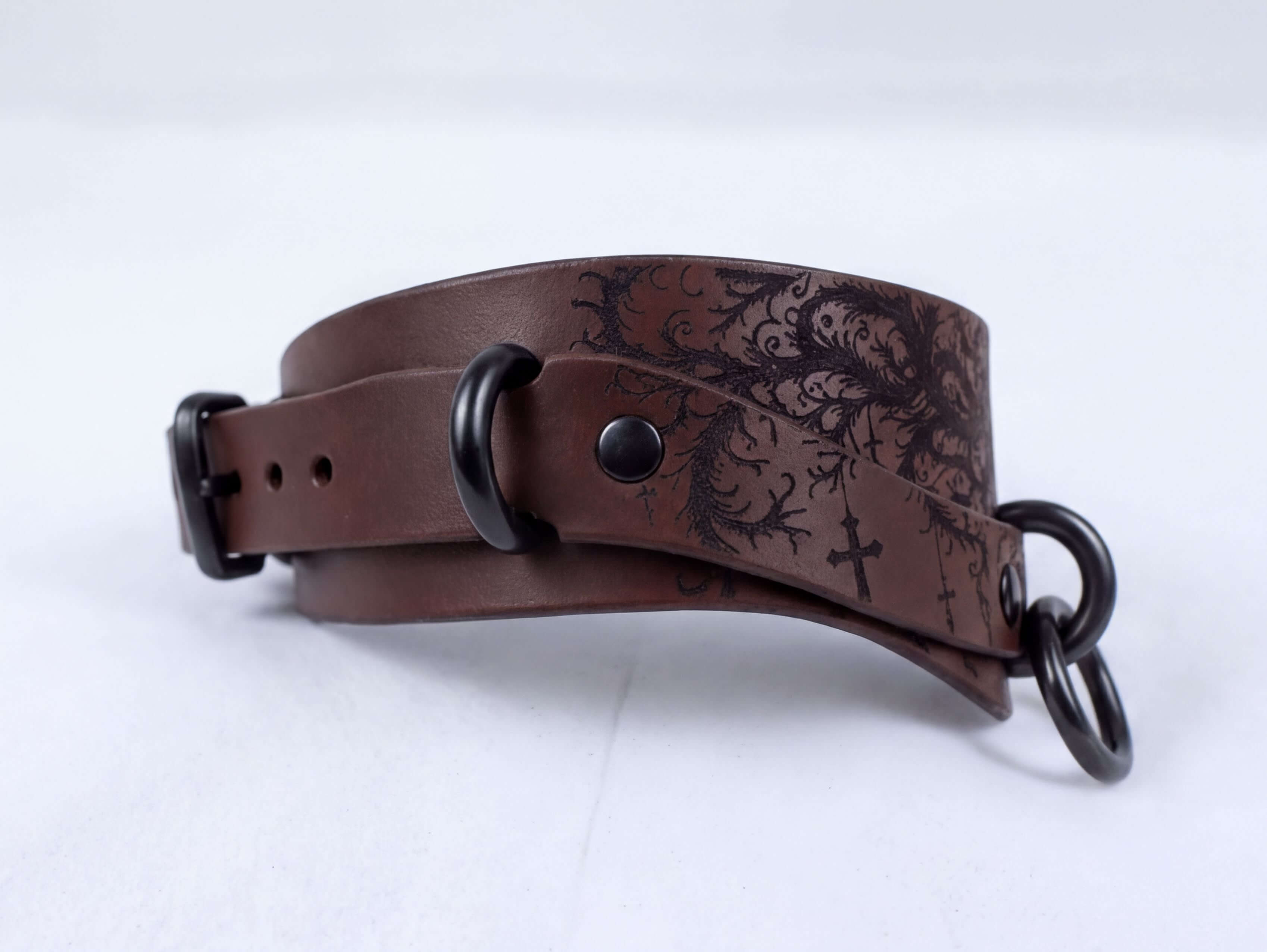 A brown leather choker necklaces with a floral pattern and metal rings on the ends.