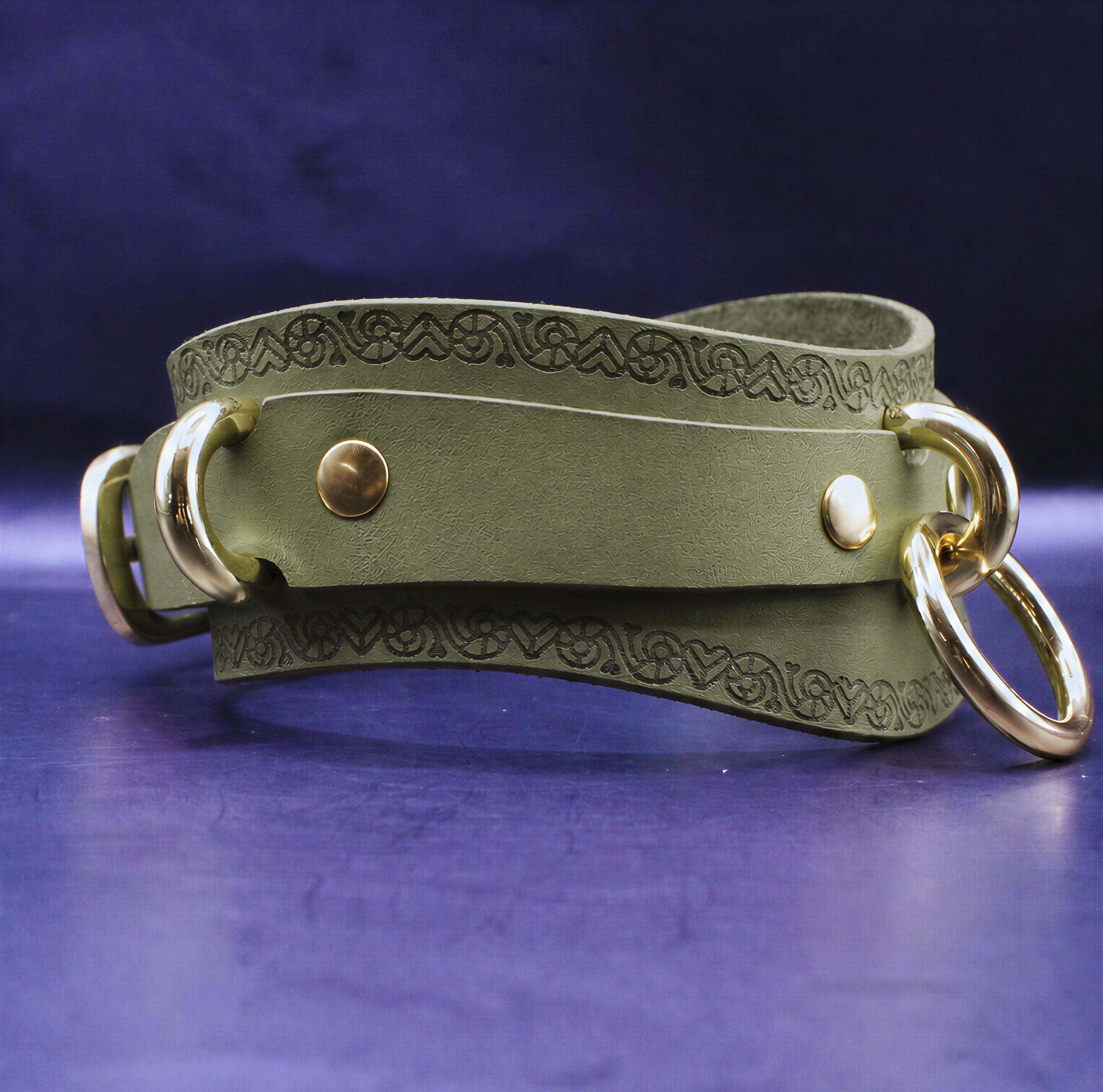 A green leather choker necklace with a decorative pattern and two gold-colored metal rings on either side.