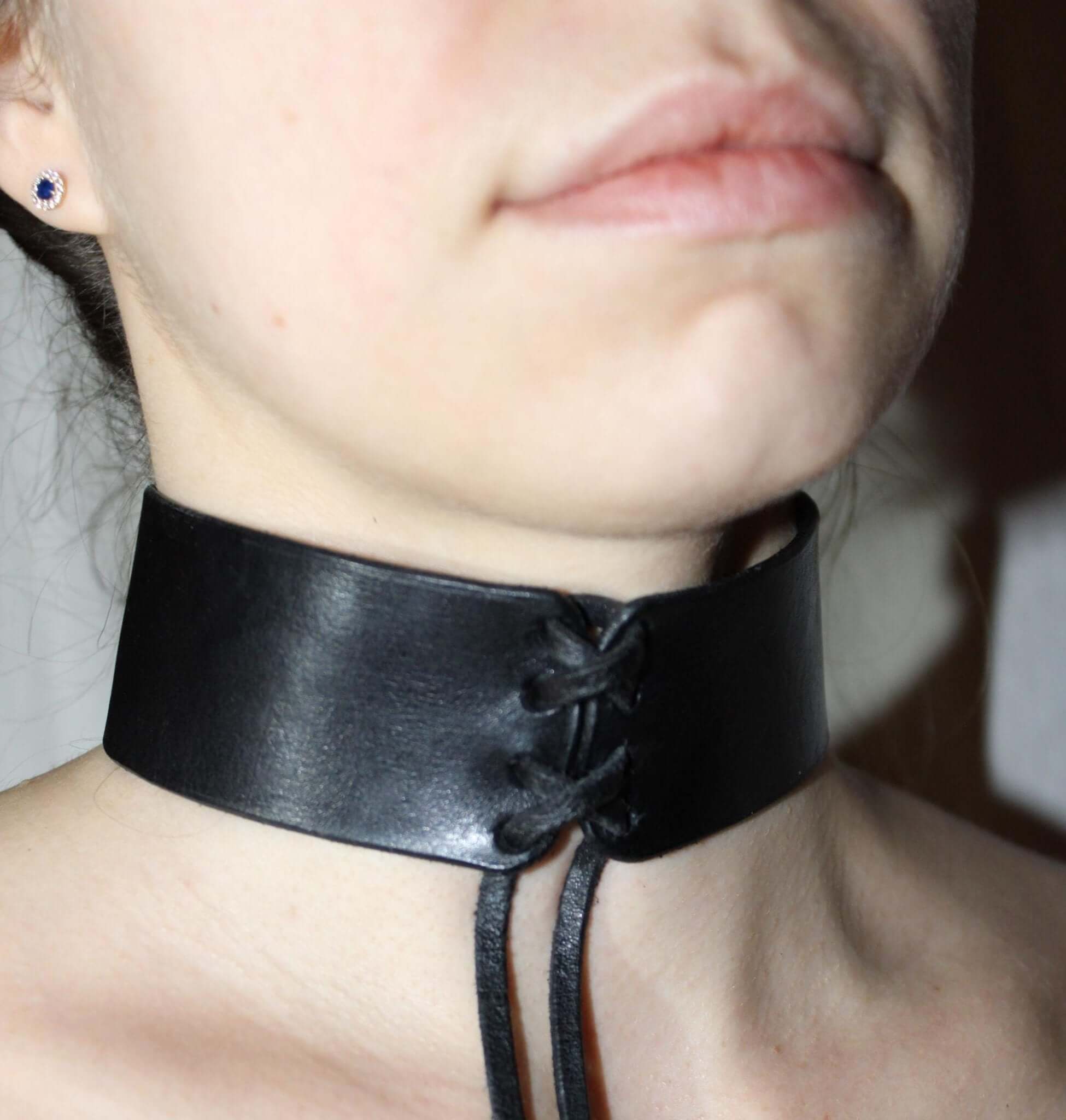 Close-up of a sleek black leather BDSM choker collar, designed for bondage and submissive play, showcasing a minimalist aesthetic.