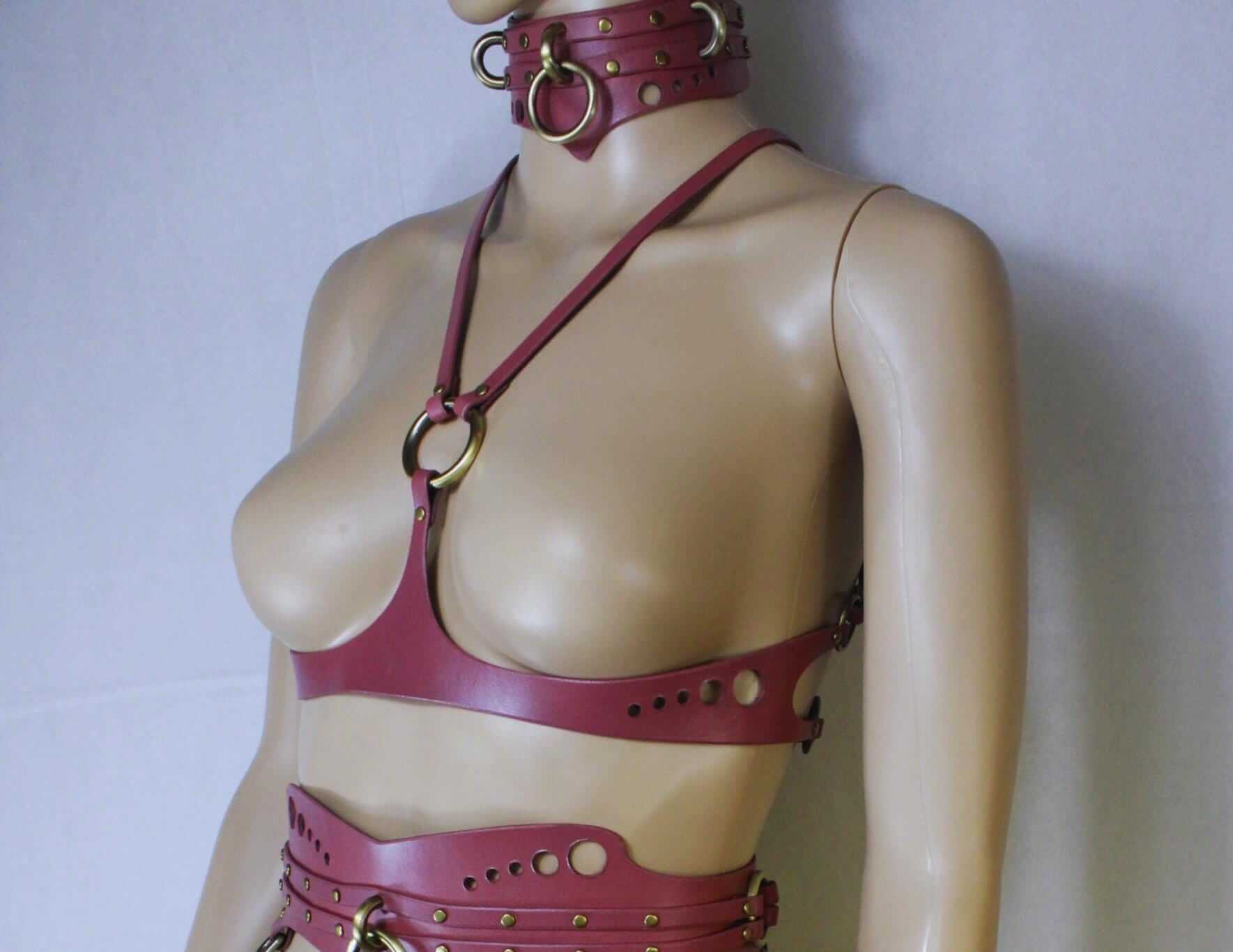 Underbust BDSM harness and collar in pink leather, accentuating curves for bondage gear, featuring rings and studs.