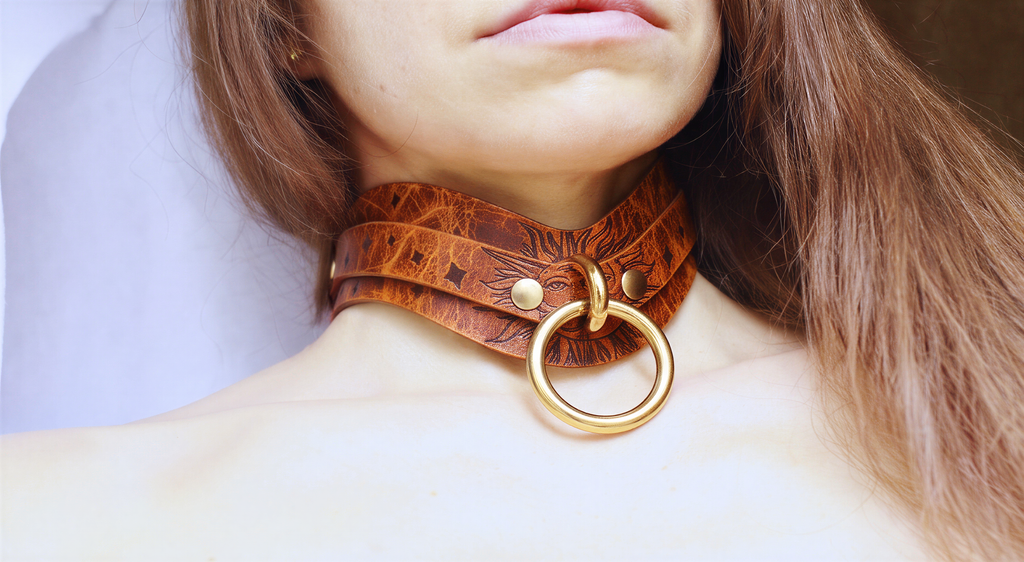 A close-up of a woman's neck and chest area, featuring a leather choker necklace with a large gold ring.