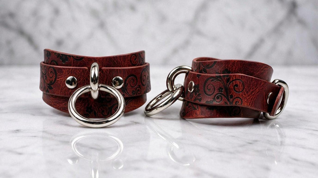 Two red leather straps with metal rings and buckles are displayed on a marble surface.