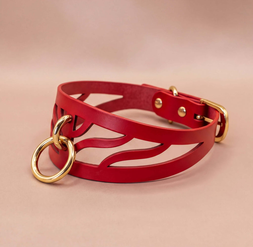 A red leather choker necklace with a cutout design and two gold-colored rings.