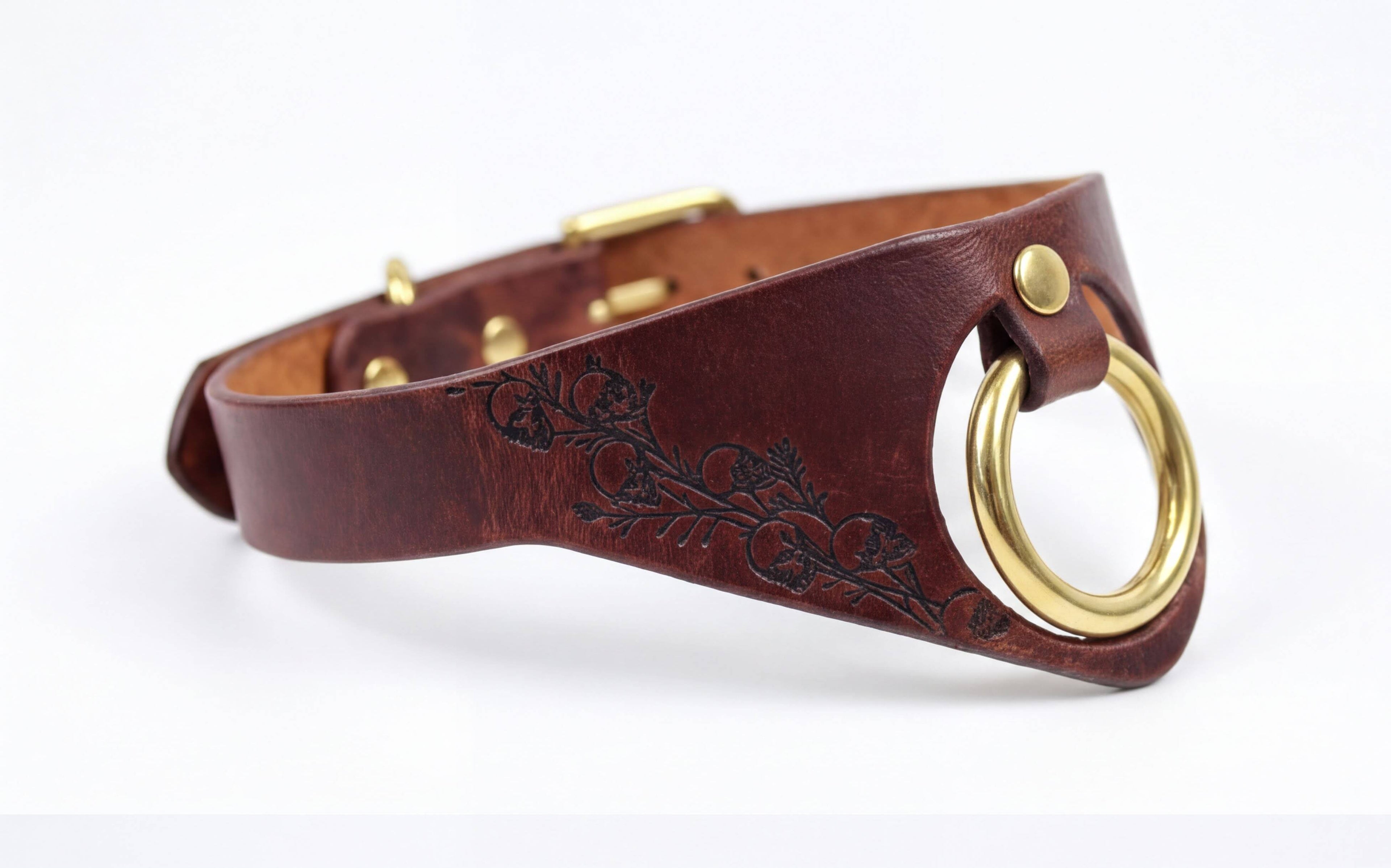 A brown leather choker collar with a gold ring and a floral design on the side.
