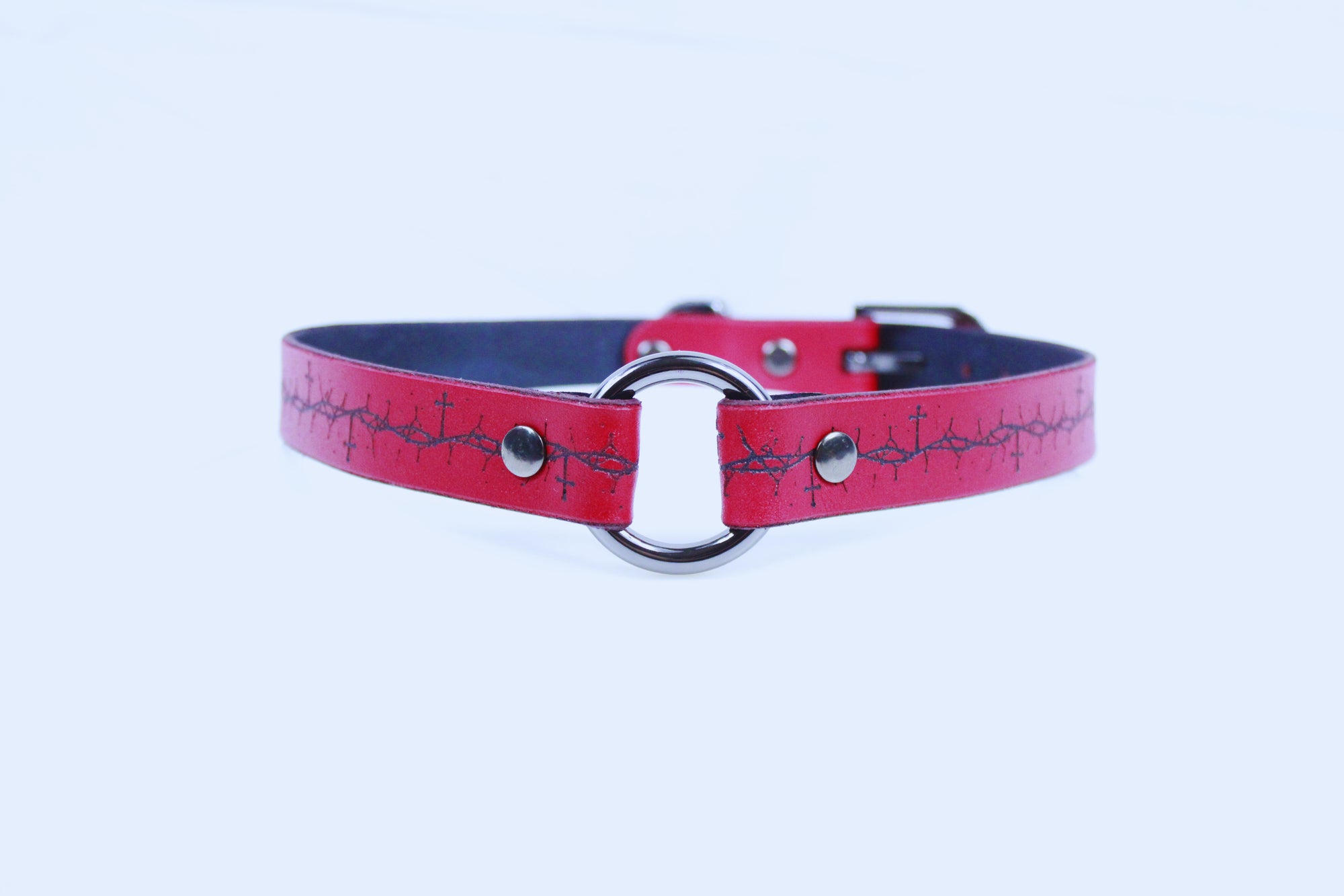 A red leather collar with a silver metal buckle and a black cross pattern on the strap.