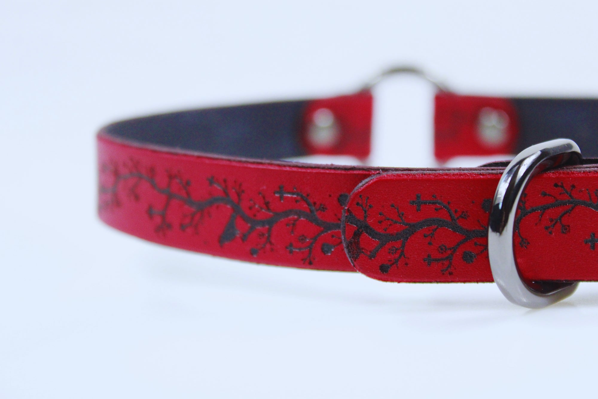 A close-up view of a red leather collar with a black tree branch design on it.