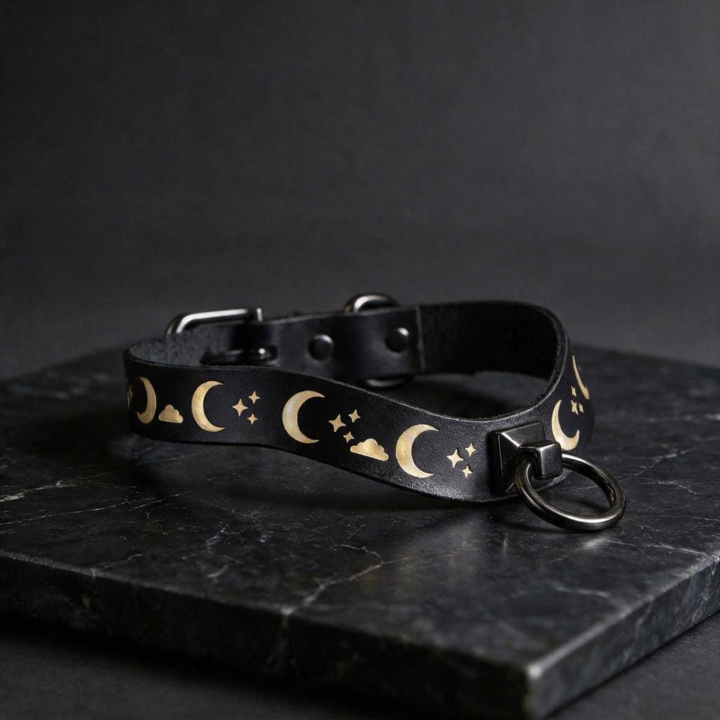 A black leather collar with a moon and star pattern design, featuring a metal ring with a clasp.