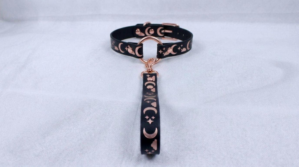 A black collar with a metallic, moon-themed design and a dangling charm.