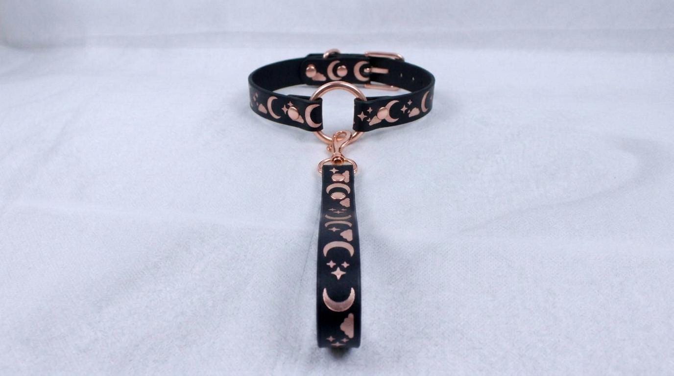 A black collar with a metallic, moon-themed design and a dangling charm.