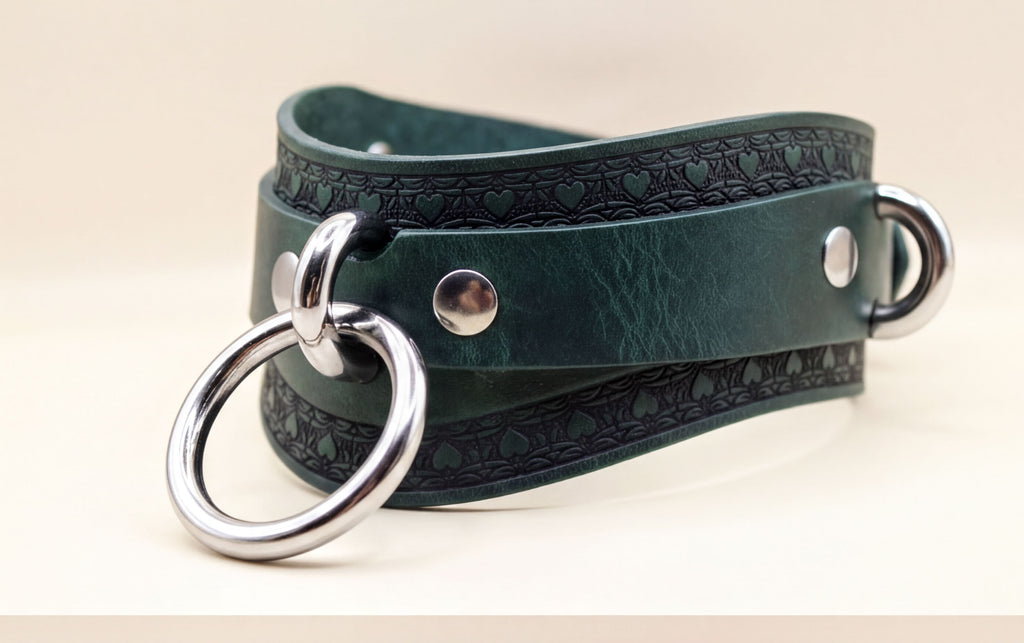A close-up view of a green leather choker necklace with metal rings and a decorative pattern on the clasp.
