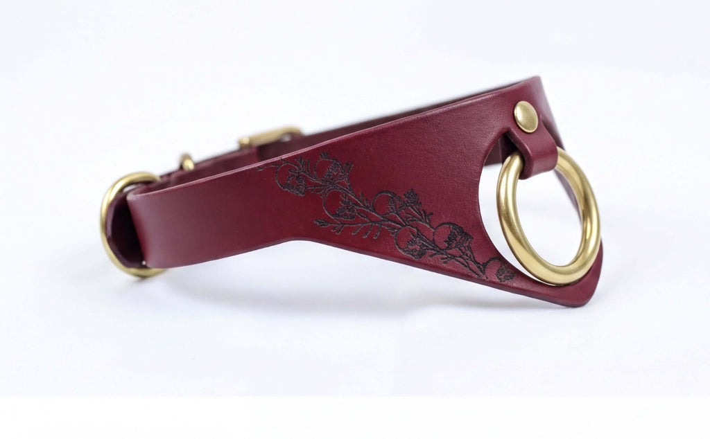 A burgundy leather collar with a gold-colored metal ring and a floral design on the side.