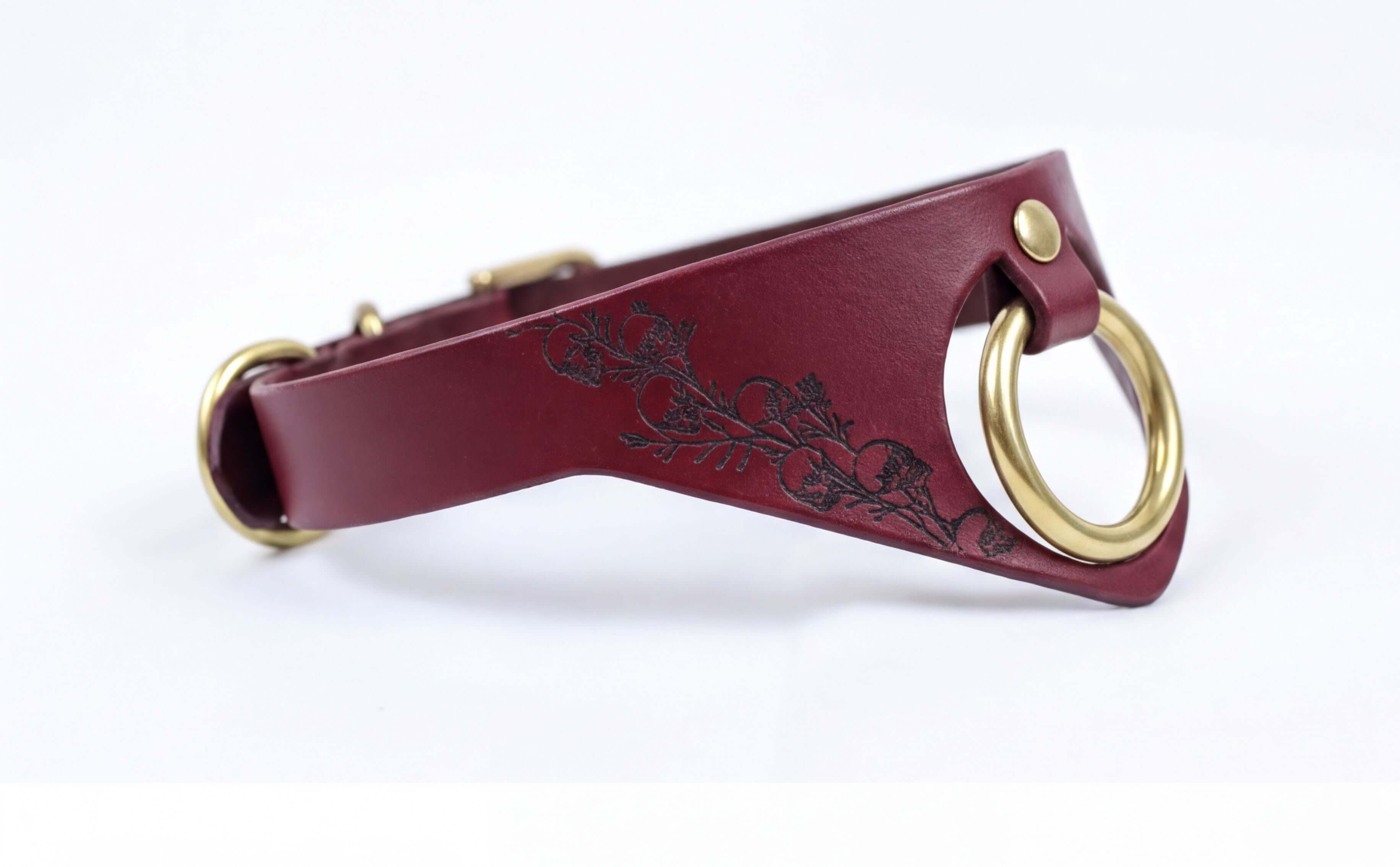 A burgundy leather collar with a gold-colored metal ring and a floral design on the side.