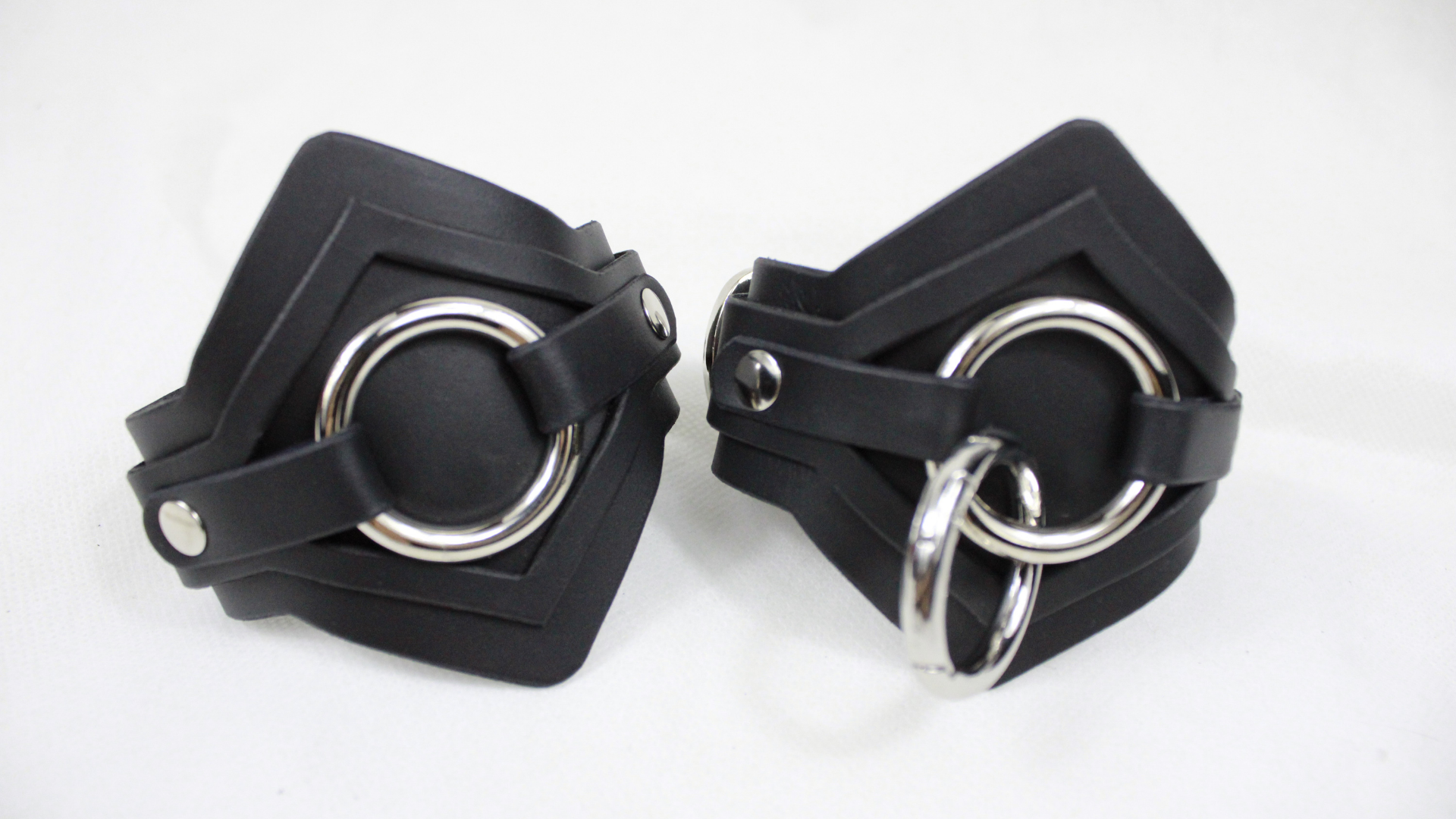 A pair of black leather cuffs with silver metal rings on them.