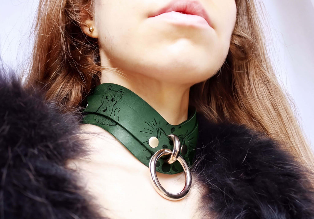 A close-up of a person wearing a green leather choker necklace with a metal ring and a cat design.