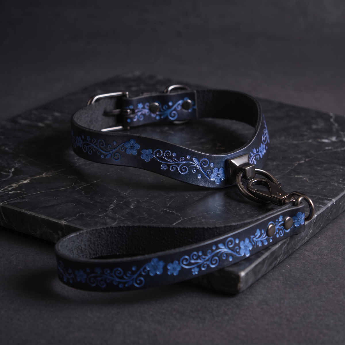 A black leather collar with a blue floral pattern and a matching leash are displayed on a dark surface.