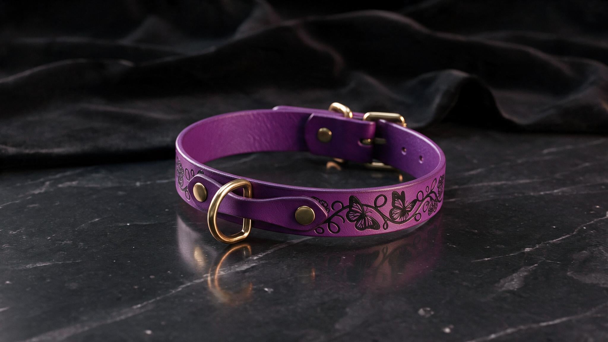 A purple leather collar with a gold buckle and decorative design is displayed on a black marble surface.