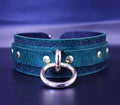 A close-up image of a green leather choker necklace with a gold-colored metal ring and decorative elements on the collar.