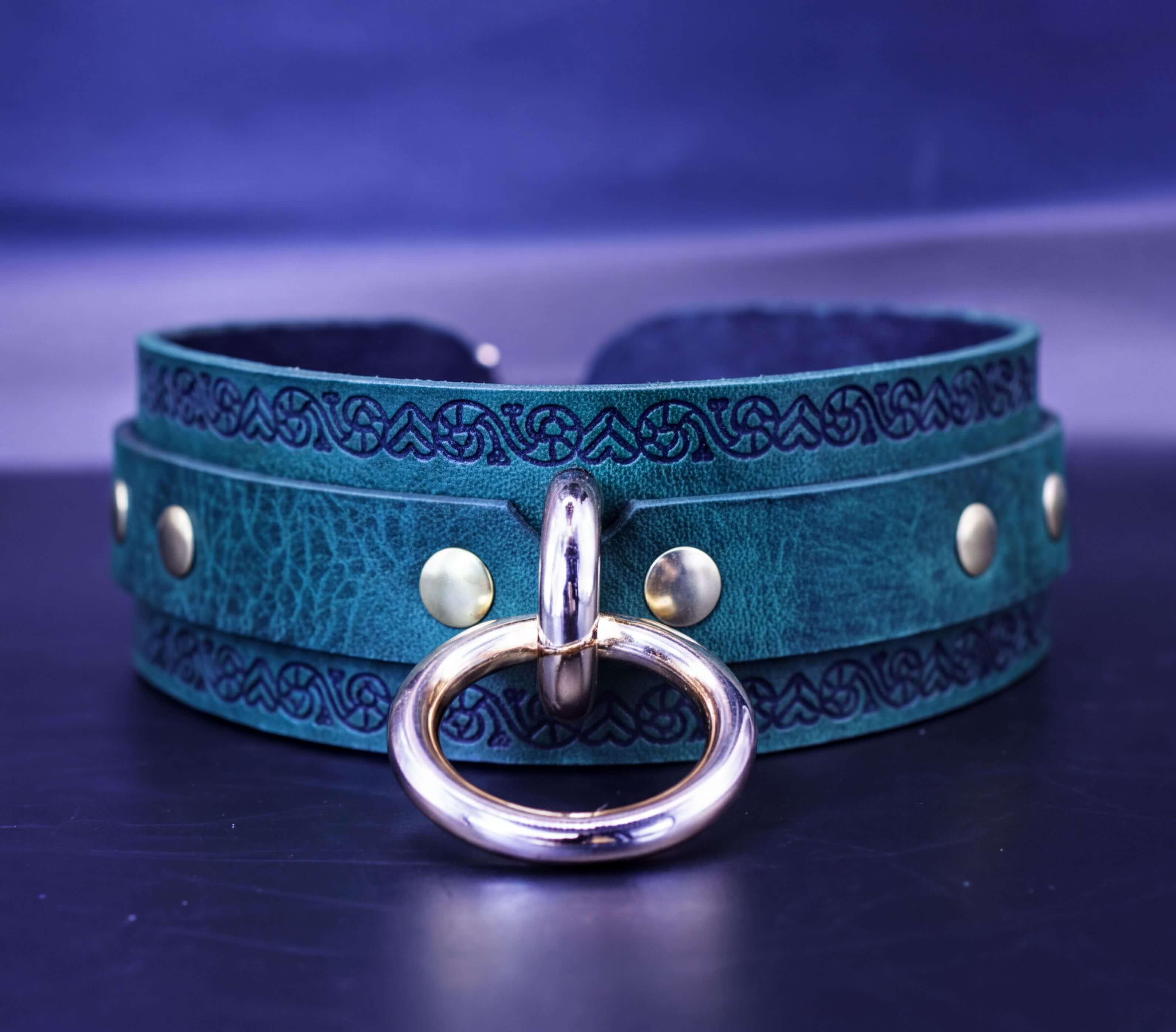 A close-up image of a green leather choker necklace with a gold-colored metal ring and decorative elements on the collar.