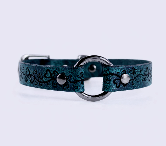 A teal-colored leather collar with a metal ring and decorative floral patterns.
