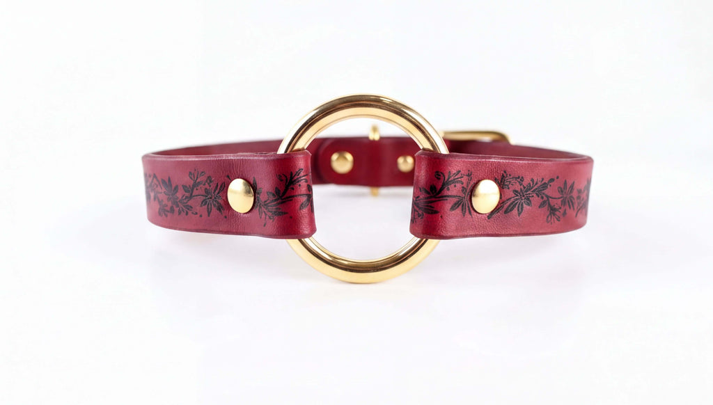A burgundy leather collar with a gold-colored circular buckle.