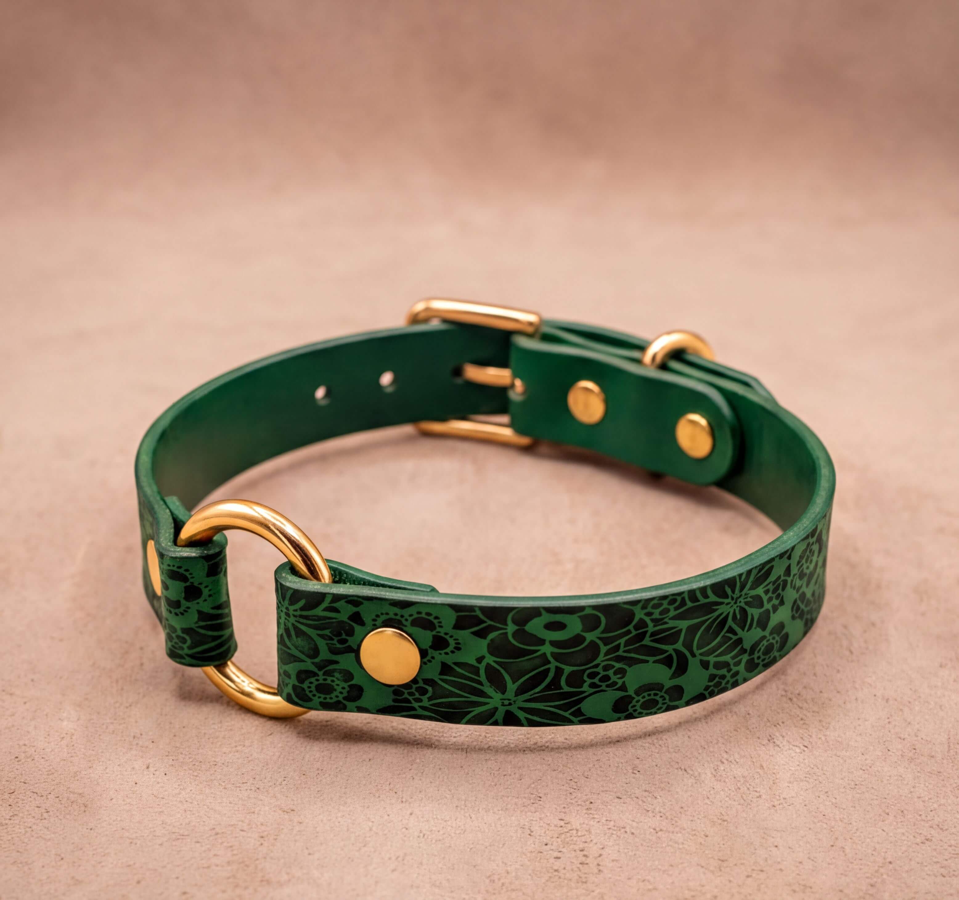 A green leather dog collar with a floral pattern and gold hardware.