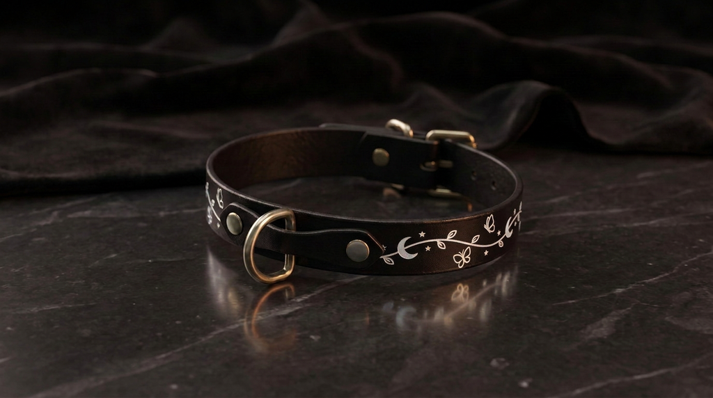 A black leather collar with a floral design on it, resting on a dark surface.