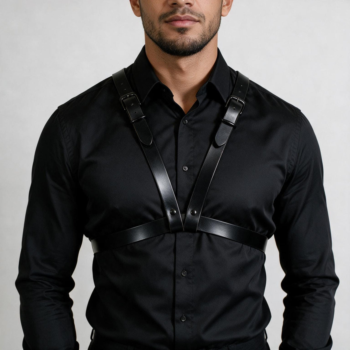 A man wearing a black shirt with a leather harness strap across his chest.