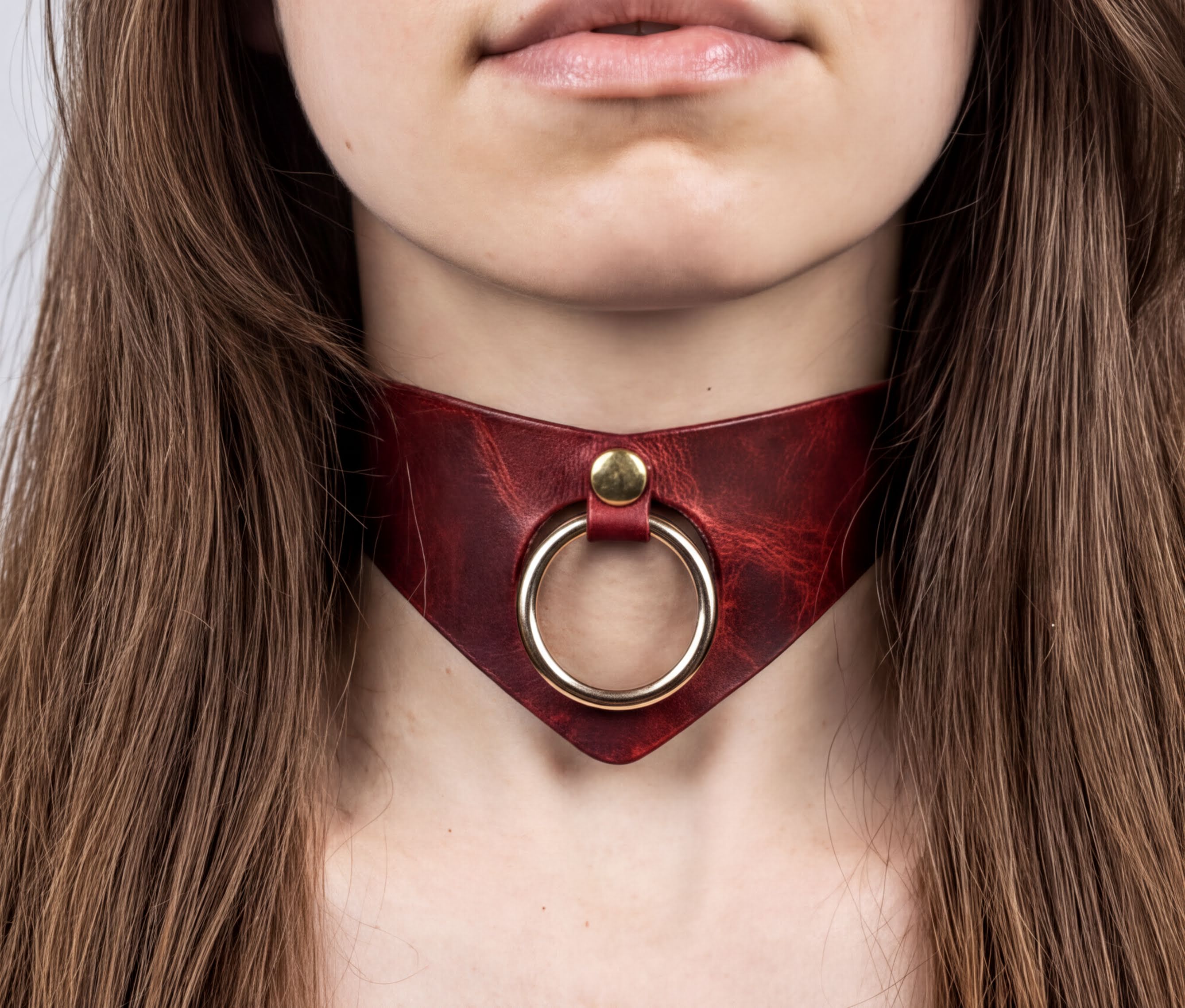 A close-up of a woman's neck and chest area wearing a red leather choker necklace with a gold ring.
