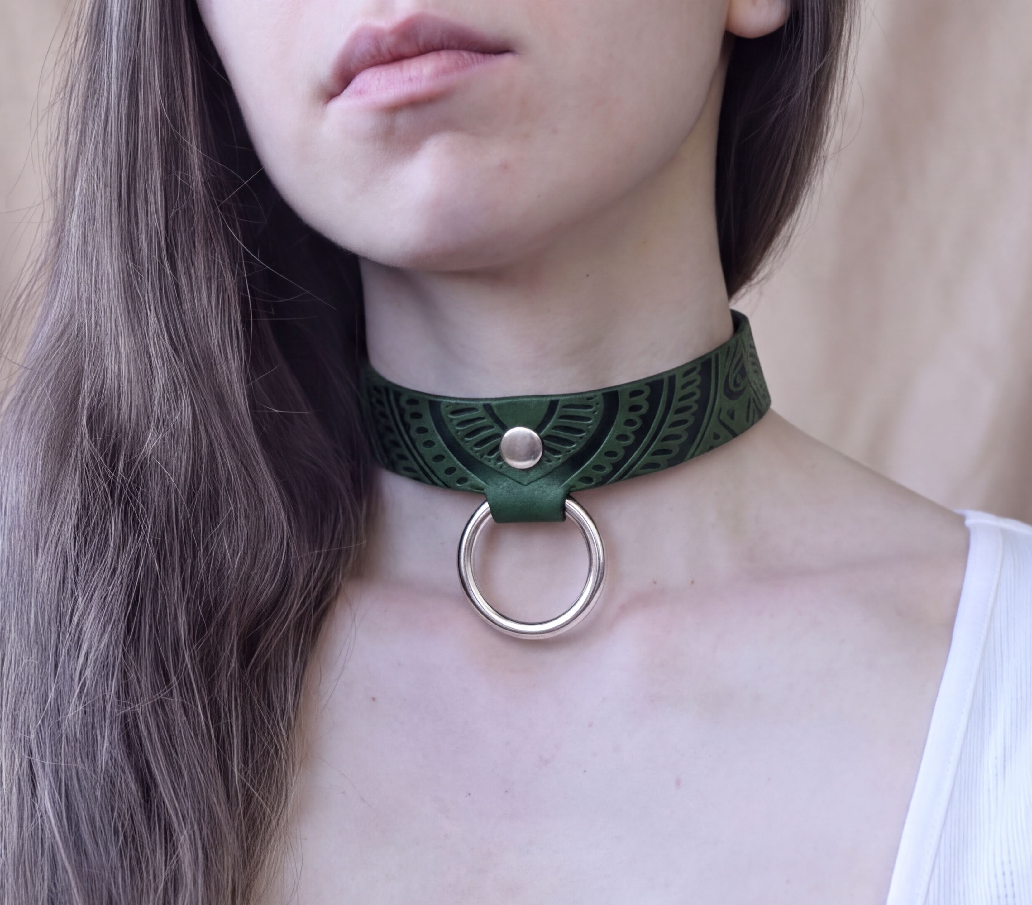 A close-up of a woman's neck and chin wearing a green choker necklace with a metal ring.