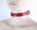 A mannequin head wearing a red leather choker necklace with a decorative pattern.