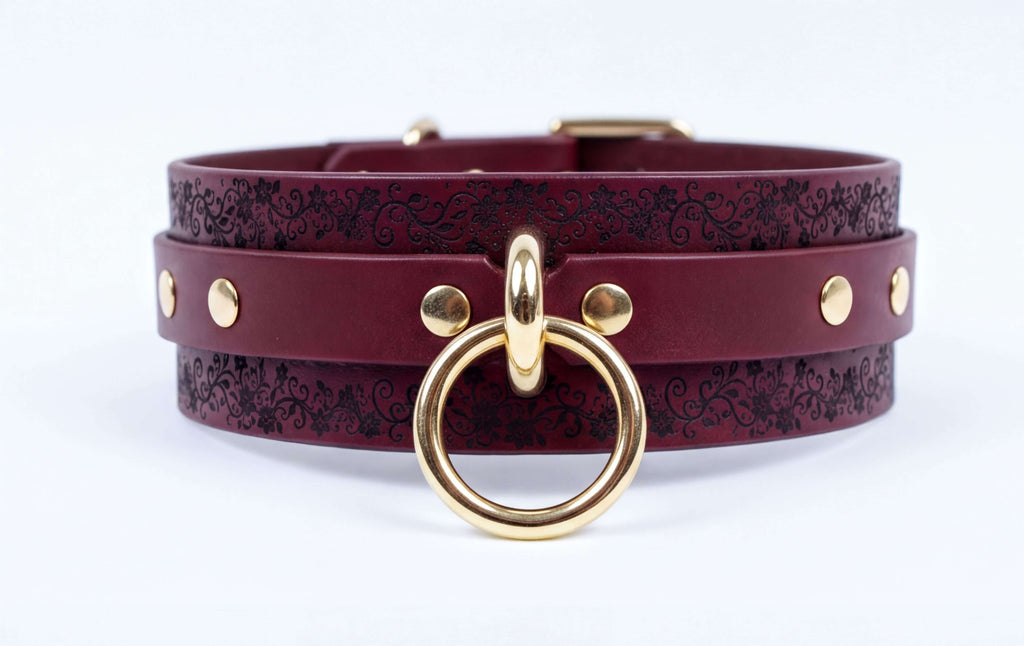 A burgundy leather choker necklace with a gold-colored metal ring and studs on the straps.