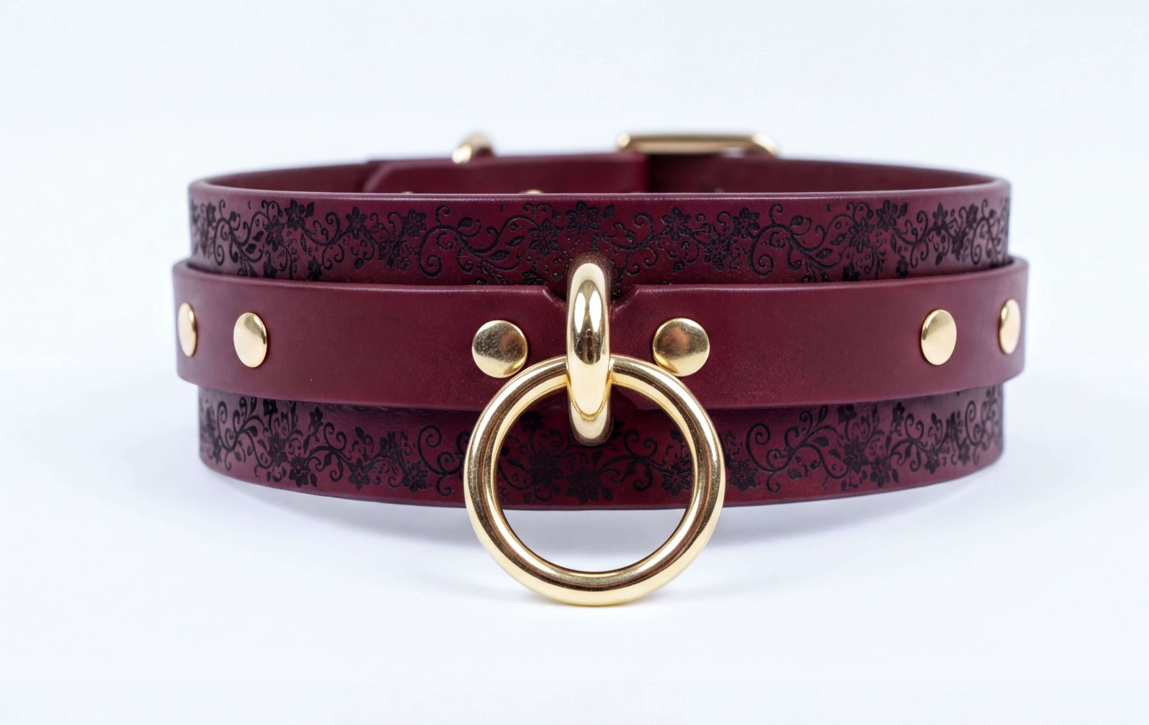 A burgundy leather choker necklace with a gold-colored metal ring and studs on the straps.