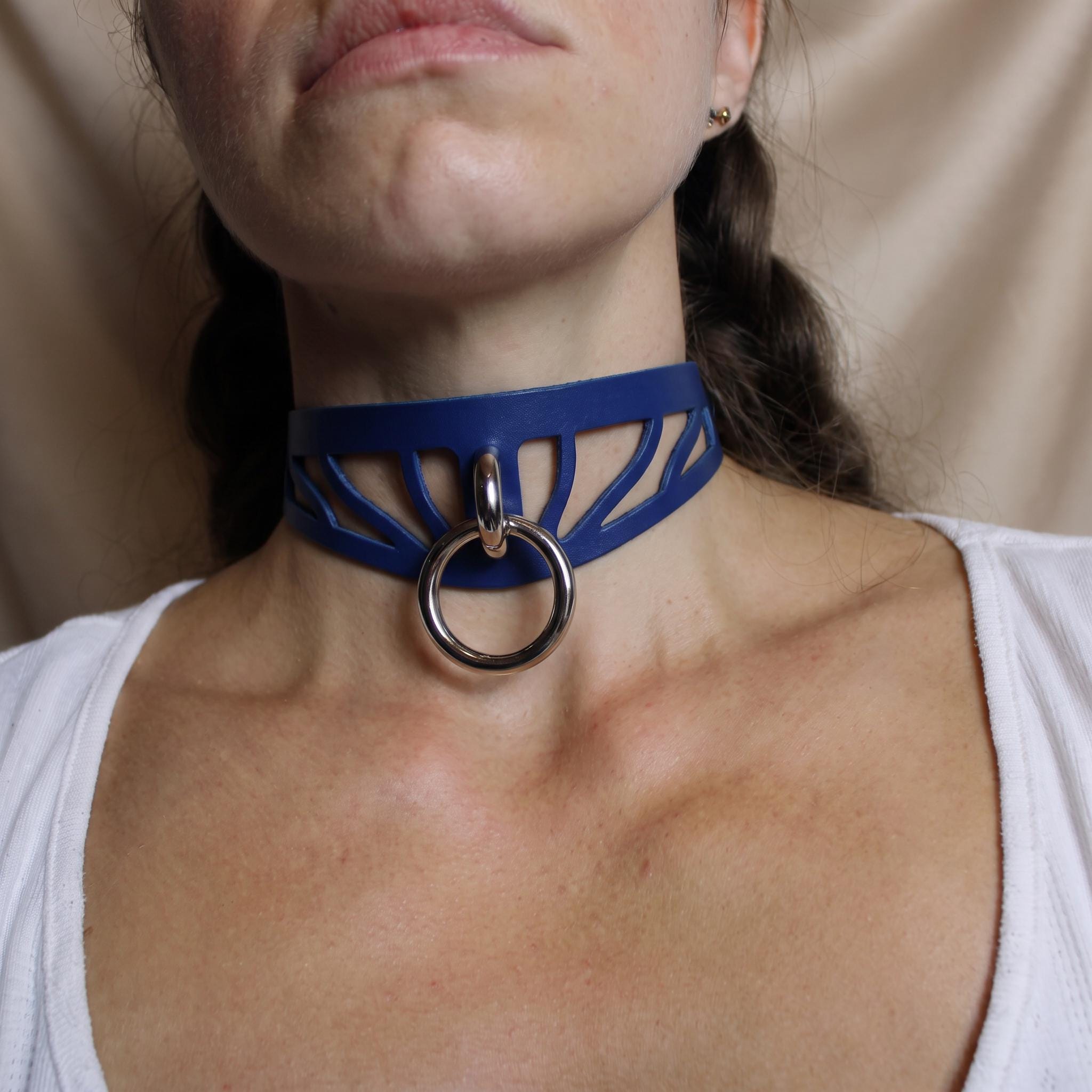 A close-up of a woman wearing a blue choker necklace with a metal ring on it.