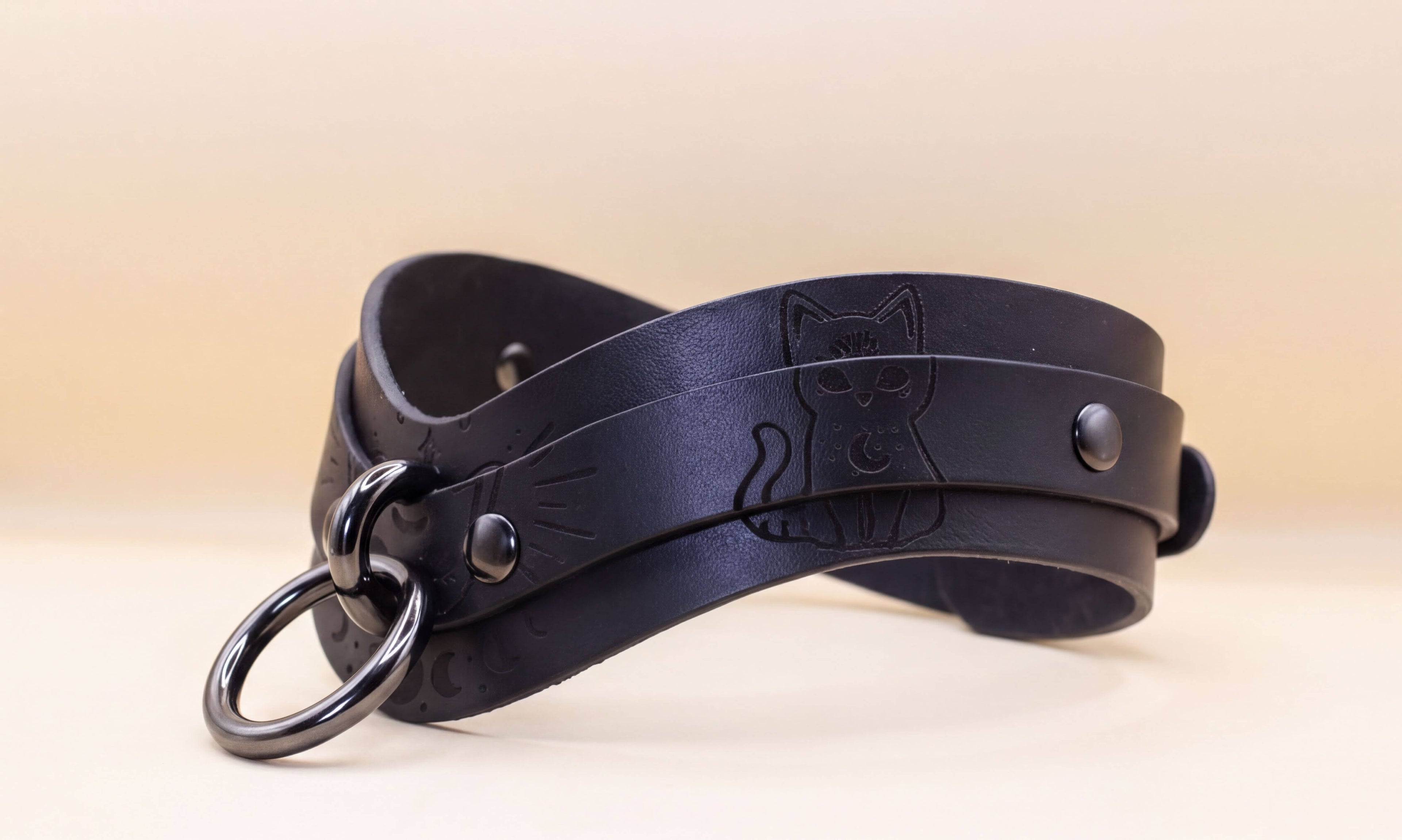 A black leather choker necklace with a cat design on the front.