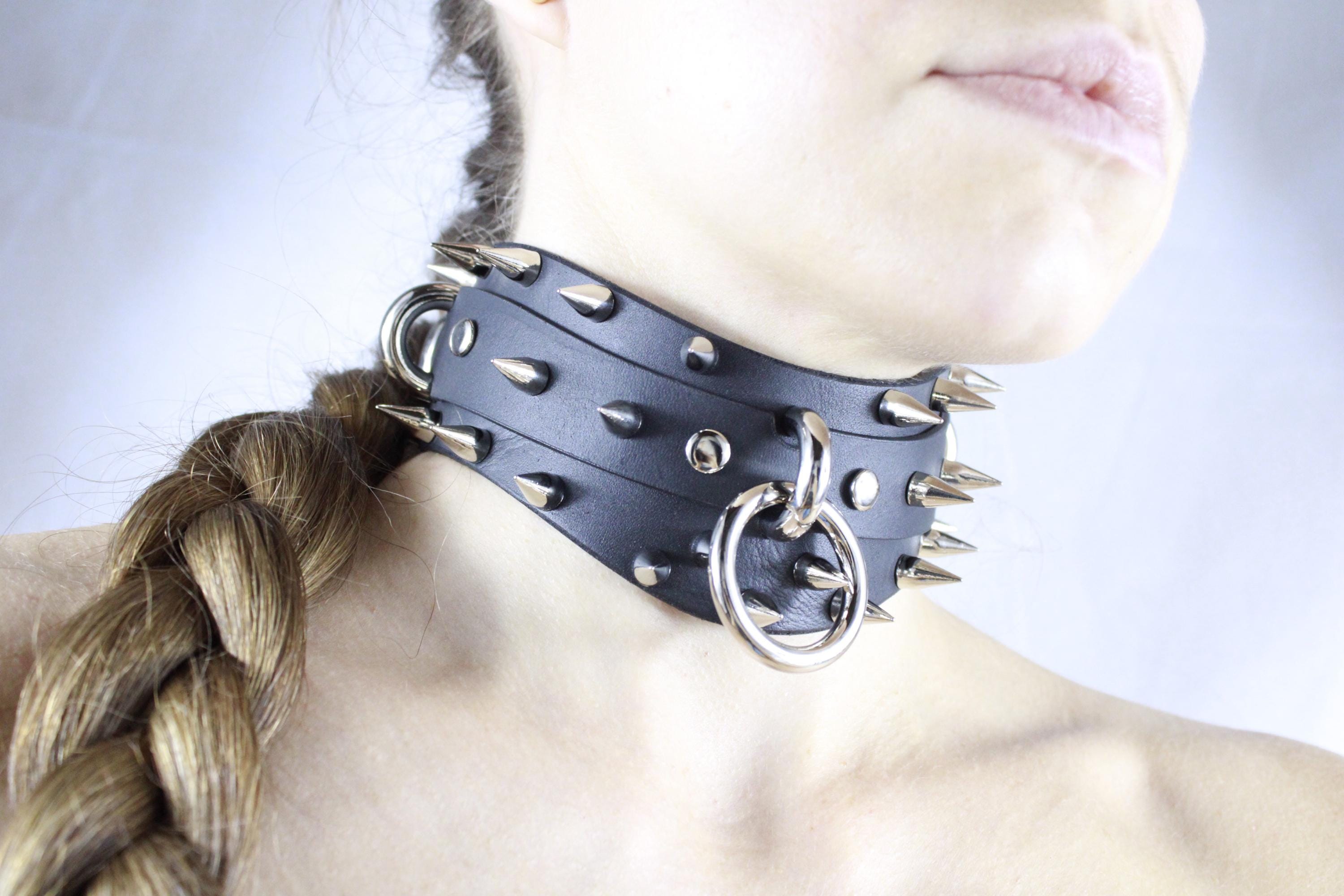 A close-up of a person wearing a black leather choker necklace with spikes and a metal ring.