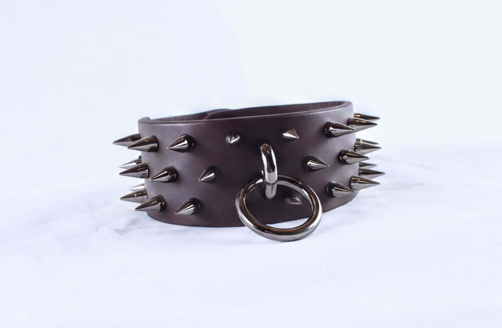 A leather bracelet with spikes protruding from it, and a metal ring attached to the bracelet.