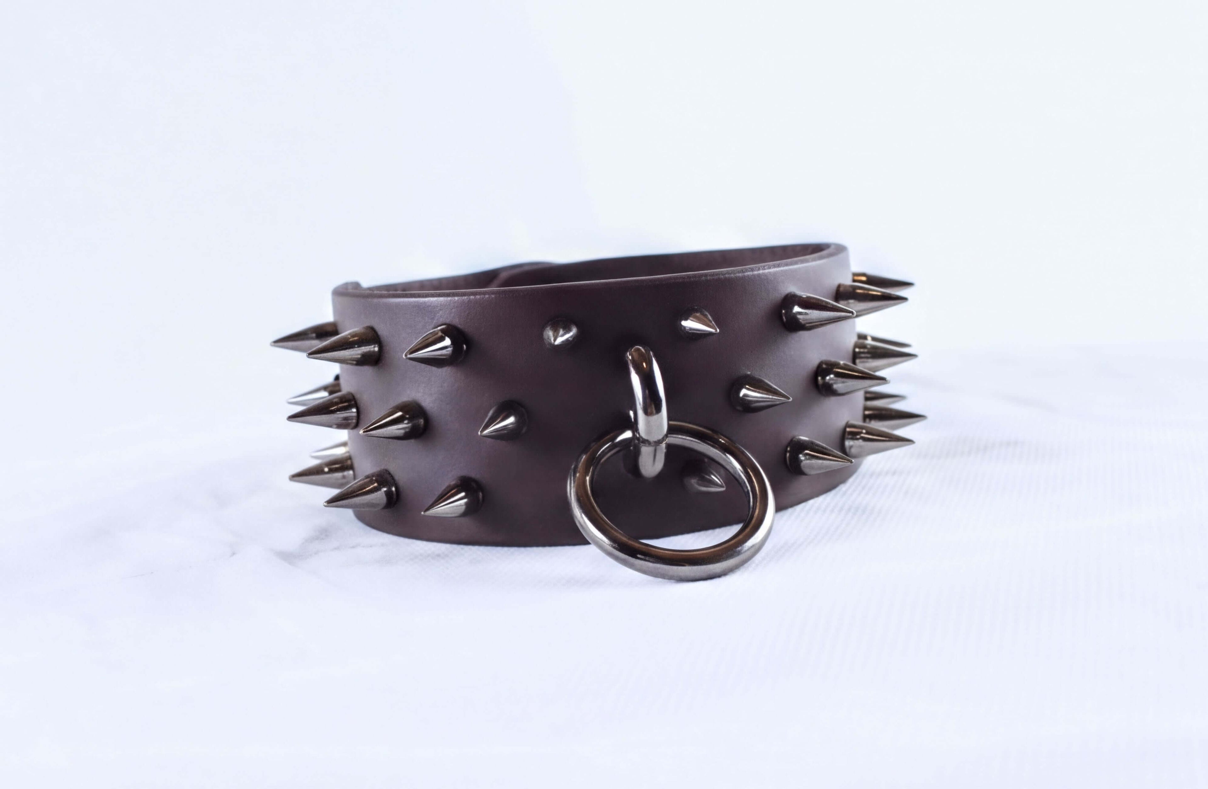 A leather bracelet with spikes protruding from it, and a metal ring attached to the bracelet.