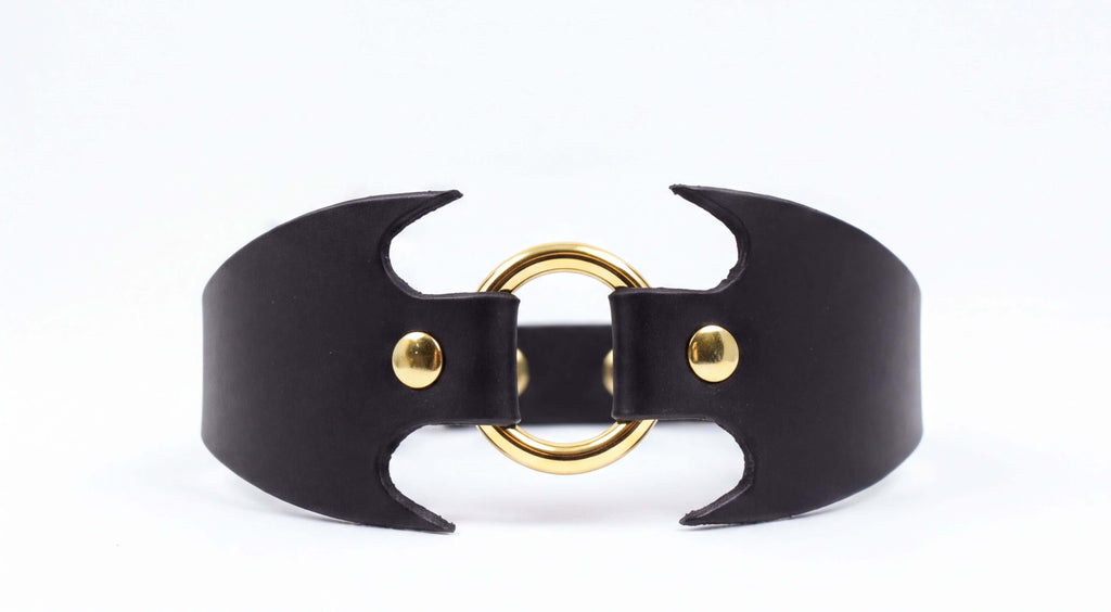 A black leather choker necklace with a gold-colored circular clasp.