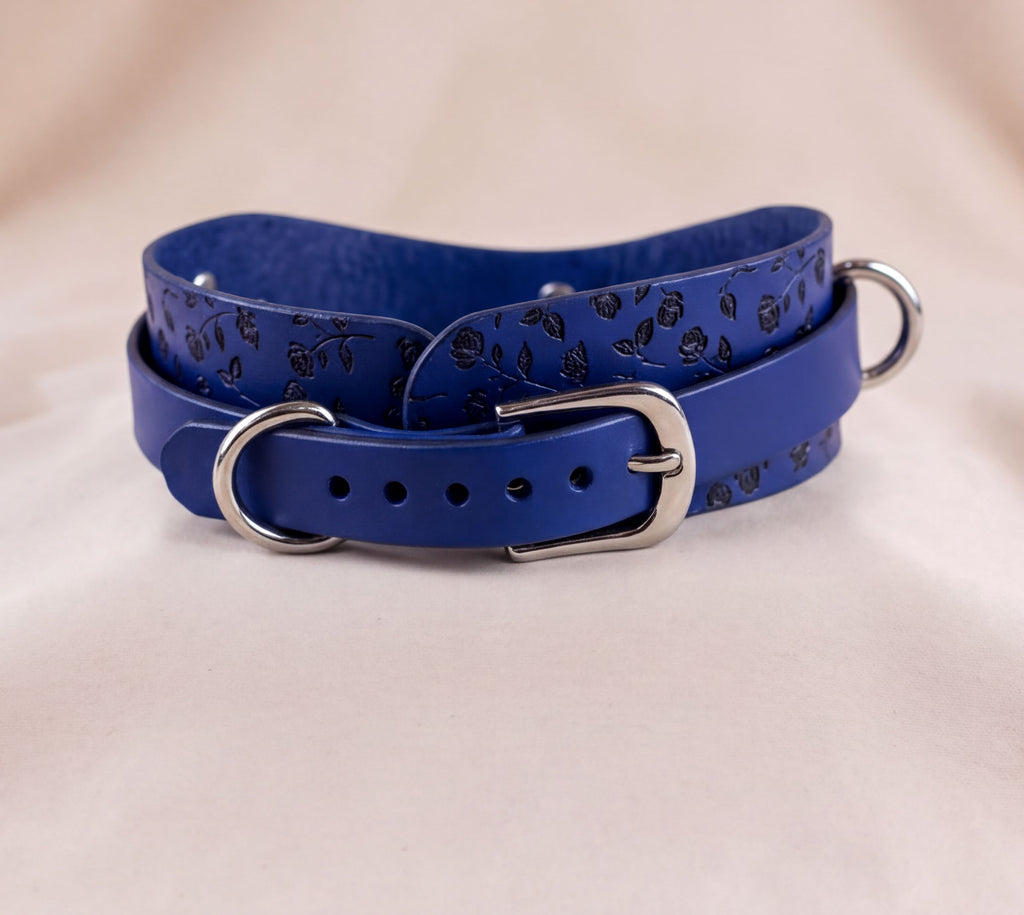 A blue leather collar with a metal buckle and a floral pattern on the strap.