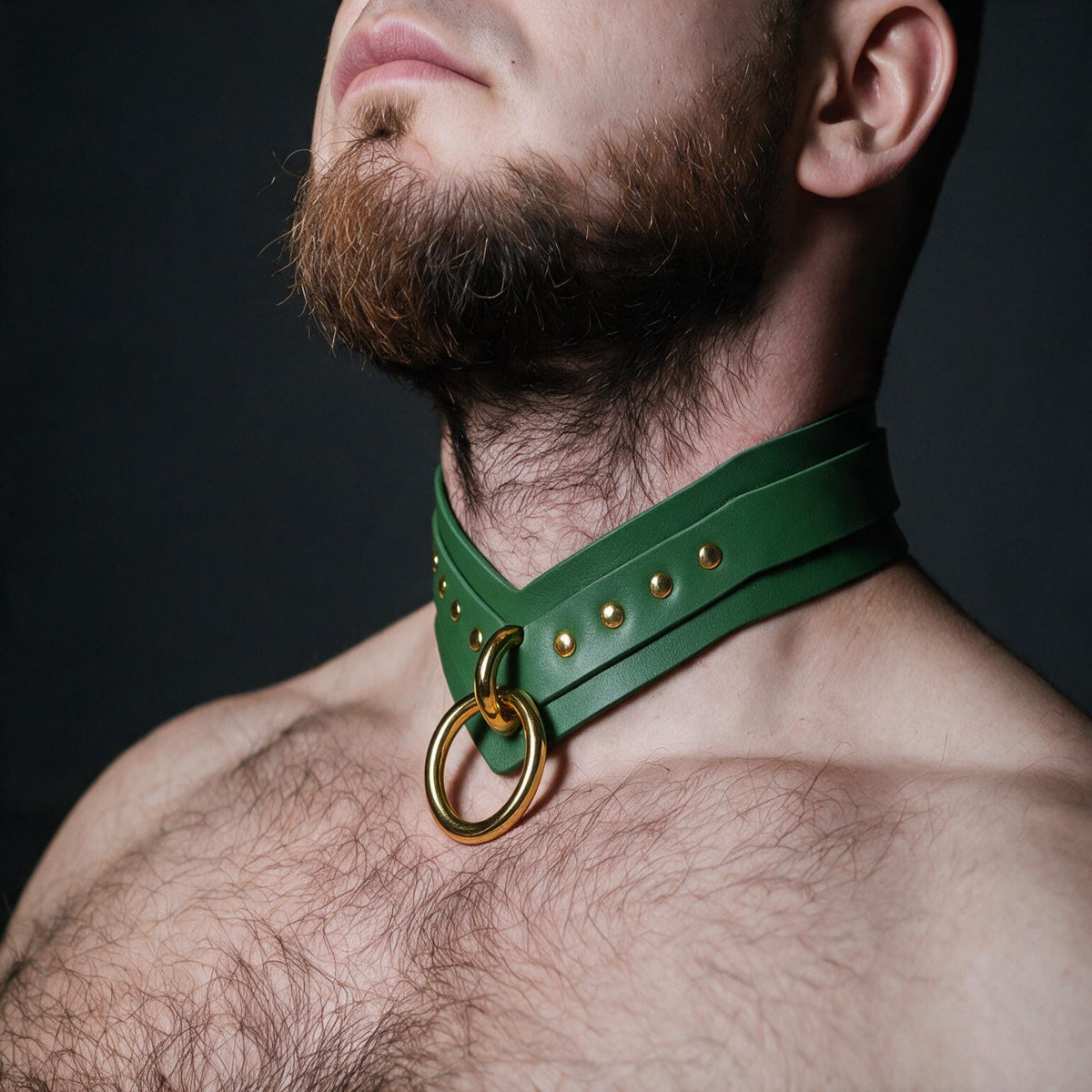 A close-up of a man's neck and chest area, with a green leather choker collar featuring a gold ring and studs.