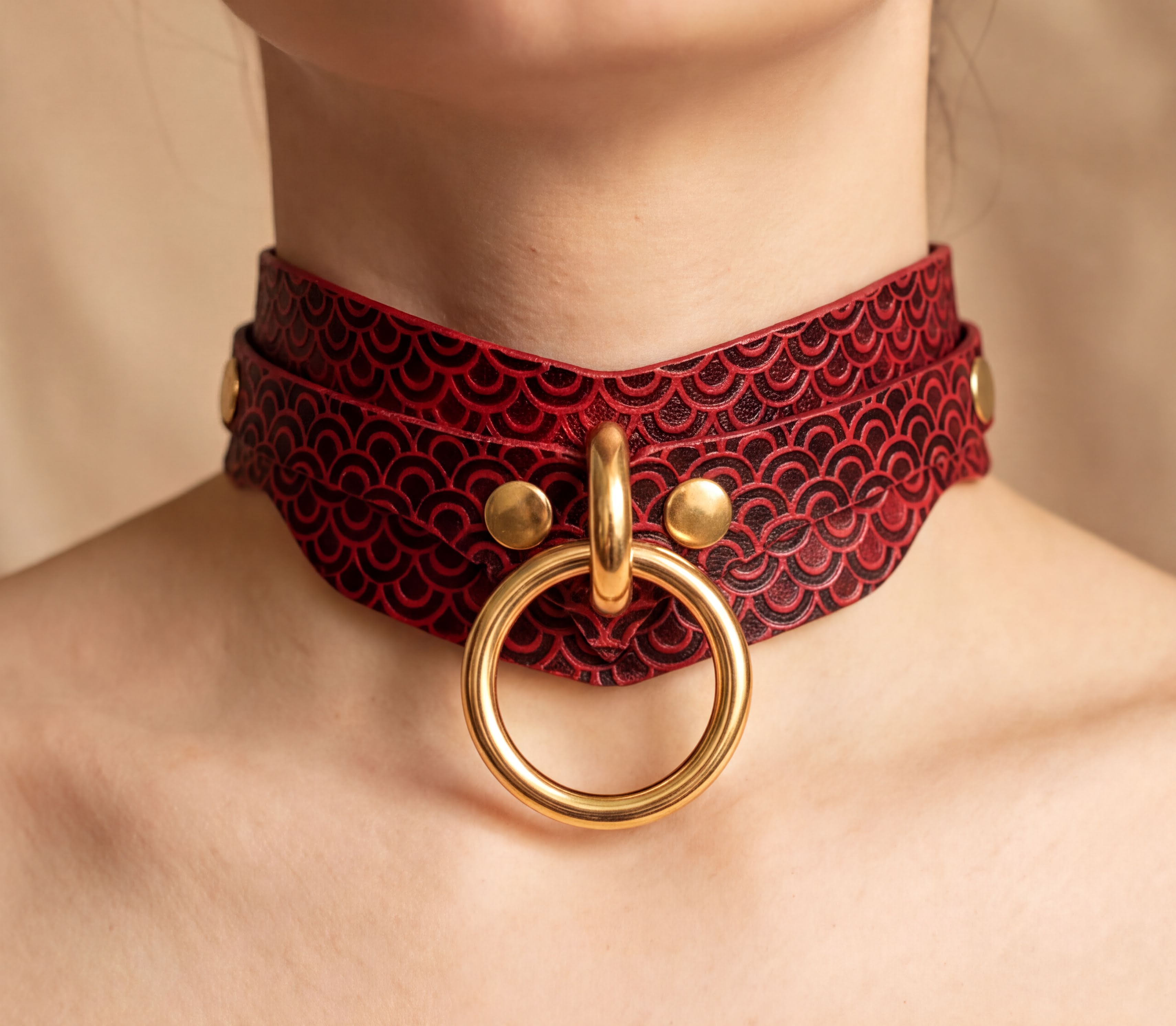 A close-up of a person's neck wearing a red and black choker necklace with a gold ring.