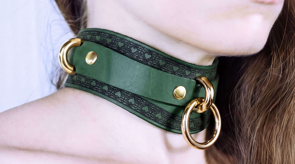 A close-up of a person's neck wearing a green leather choker with gold rings and a decorative pattern.