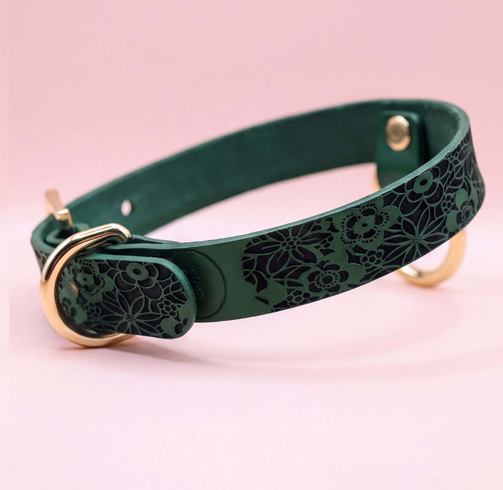 A green leather collar with a floral pattern on it, featuring a gold buckle.