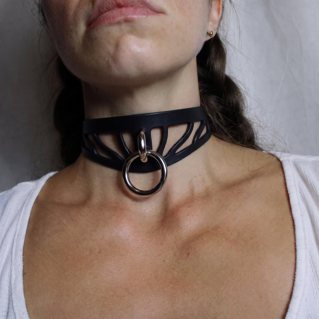 A close-up of a woman's neck and chest area wearing a black choker necklace with a metal ring.