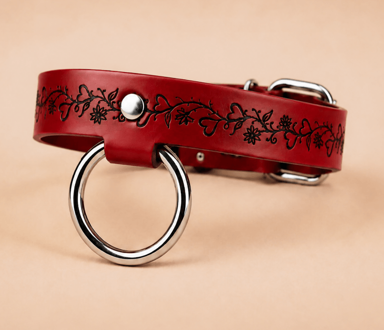 A red leather collar with a silver ring and floral design on it.