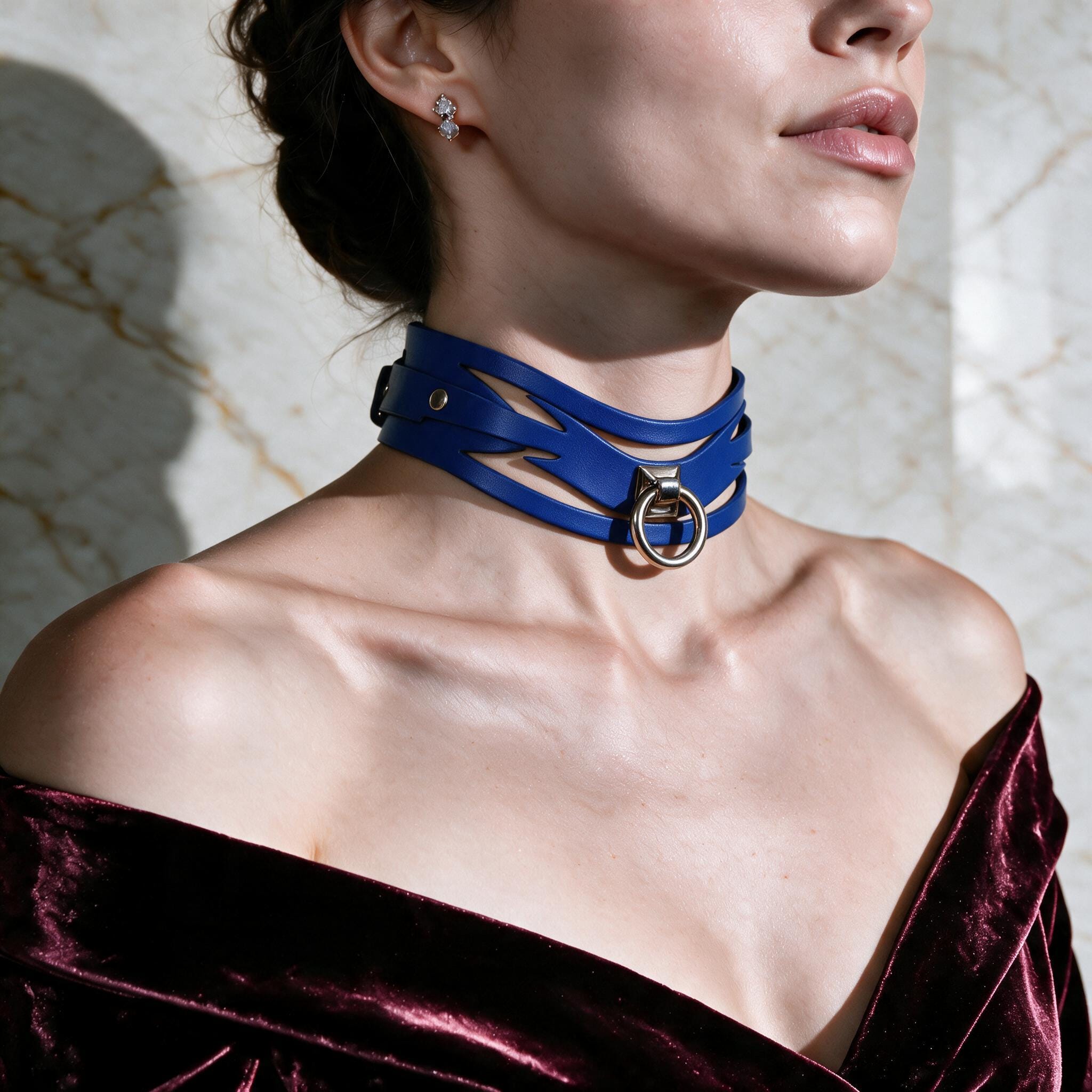 A woman wearing a blue choker necklace with a metal ring and a burgundy velvet off-the-shoulder dress.