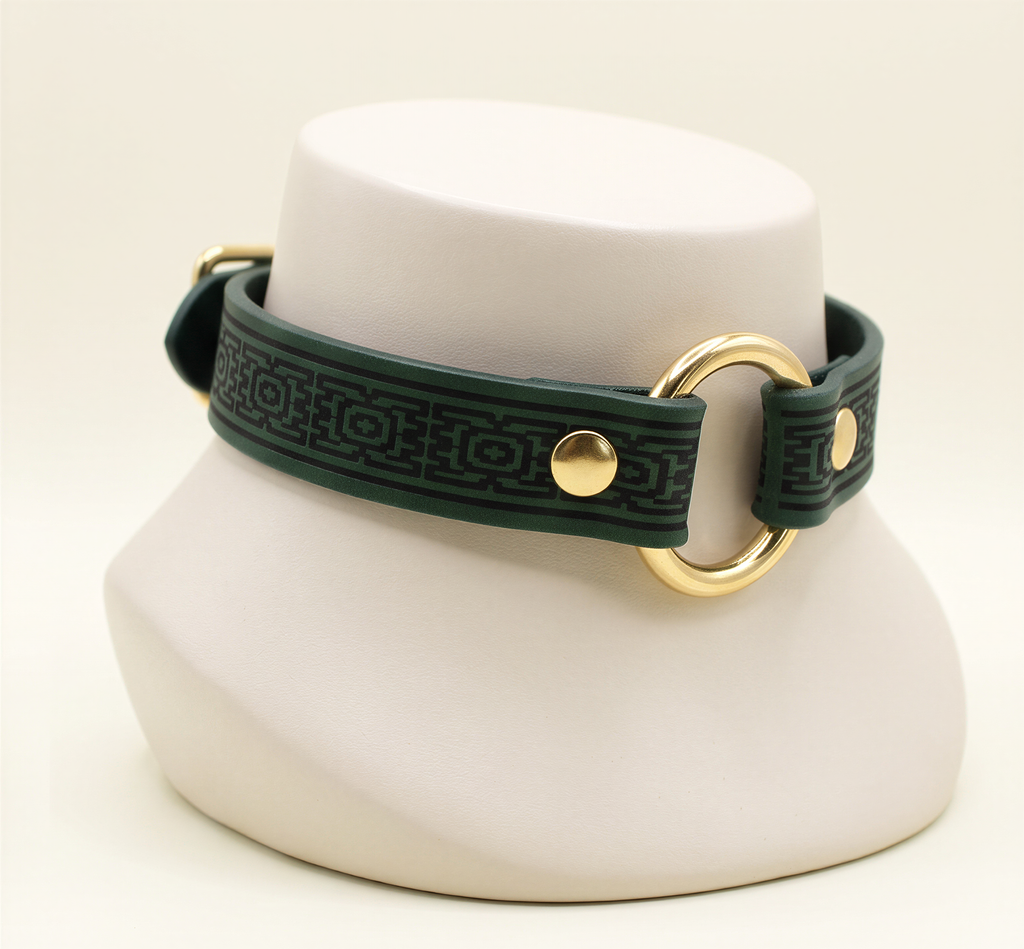 A green leather choker necklace with a gold-colored circular clasp and a geometric pattern on the strap.