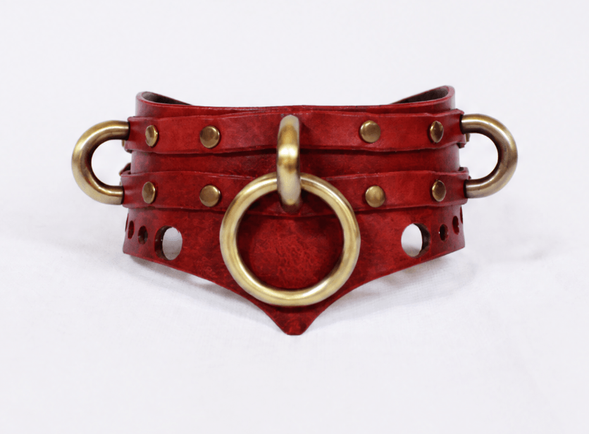 A red leather choker necklace with brass-colored metal rings and studs, creating a bold and eye-catching accessory.