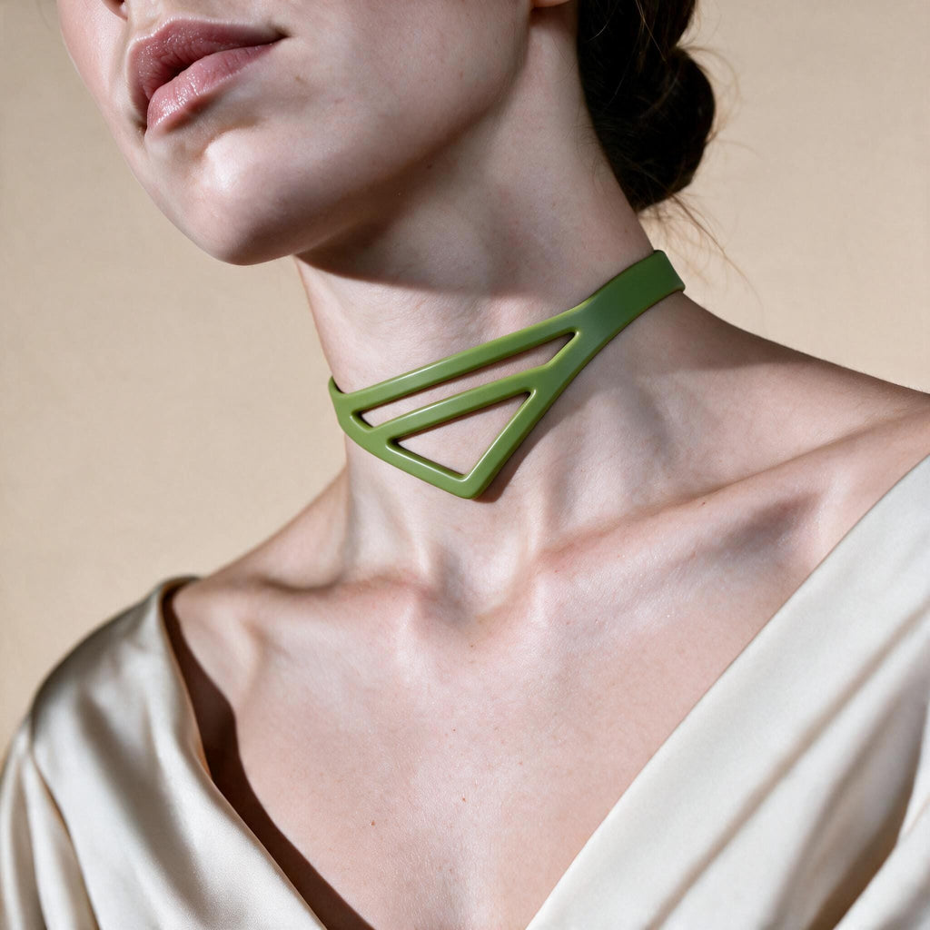 A close-up of a woman's neck and chest area, with a green geometric necklace visible.