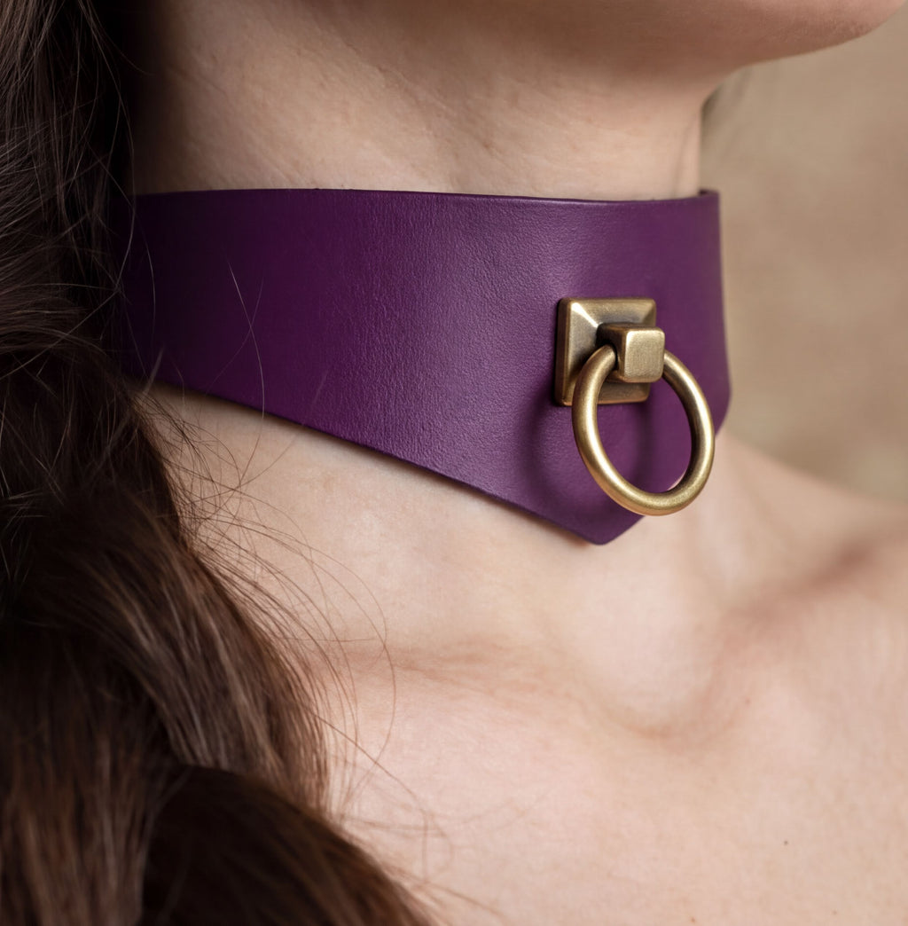 A close-up view of a person's neck and chin area, featuring a purple choker necklace with a gold-colored metal ring.